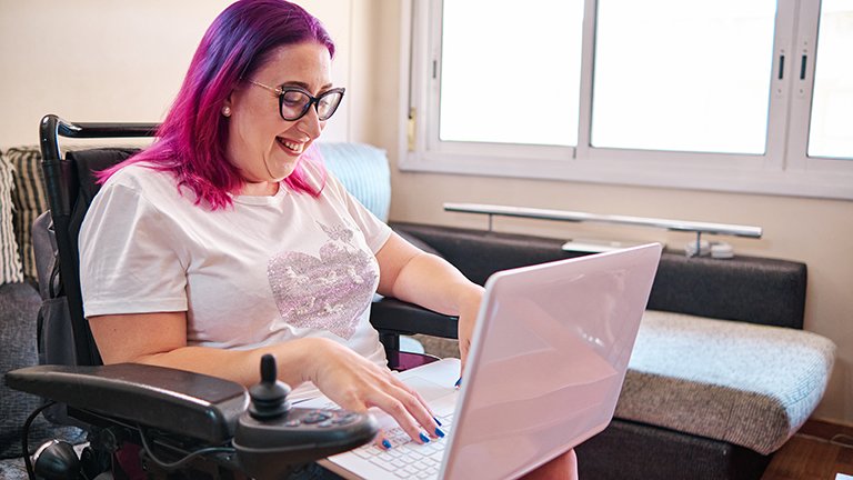 adult woman with disabilites in a wheelchair working at home with laptop