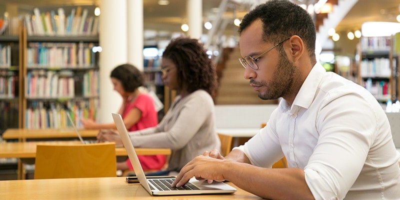 Young male student studying in library on laptop