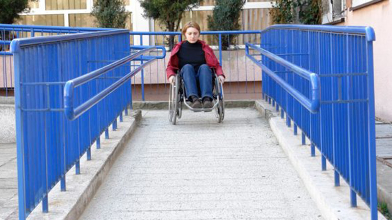 A white woman rolls her wheelchair down an accessible ramp