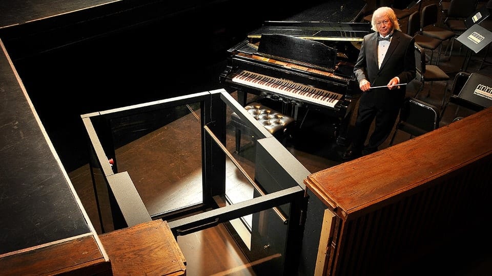 Ascension Protege Wheelchair Lift sits beside a raised stage where a orchestra conductor stands beside a piano