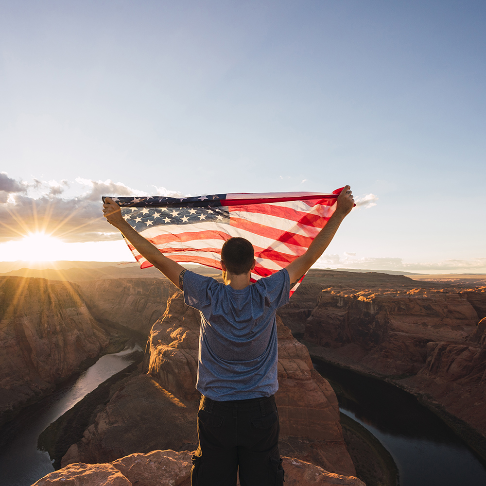 USA, Arizona, Colorado River, Horseshoe Bend, young man on viewpoint with American flag